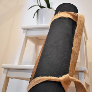 May include: A black yoga mat rolled up and secured with a natural jute strap. The mat is resting on a white wooden step stool.
