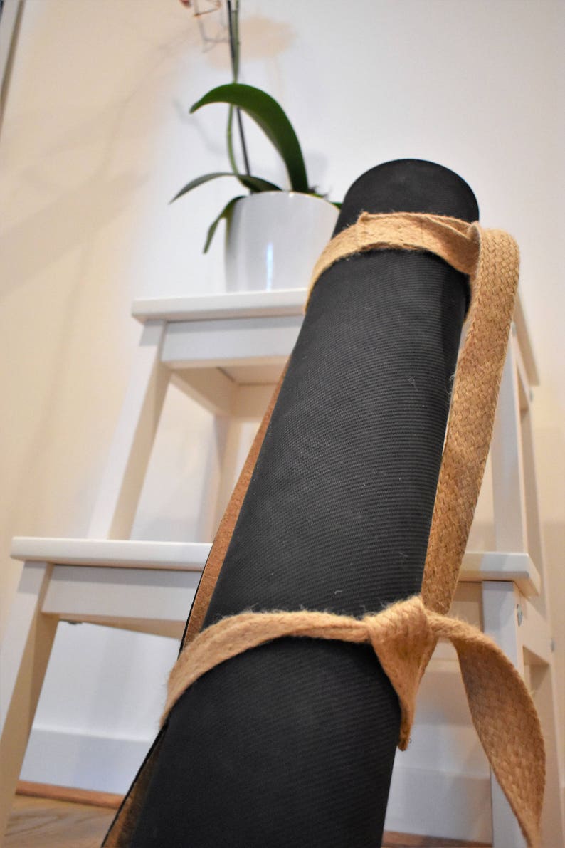 May include: A black yoga mat rolled up and secured with a natural jute strap. The mat is resting on a white wooden step stool.