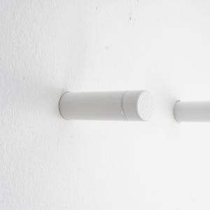 May include: Two white cylindrical wall hooks with rounded ends. The hooks are mounted on a white wall.