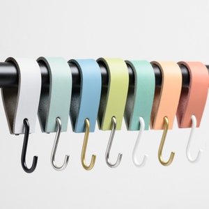 May include: A set of eight leather-wrapped hooks in various pastel colors, including white, light blue, green, yellow, and peach. Each hook is attached to a black metal rod and has a metal hook at the bottom.