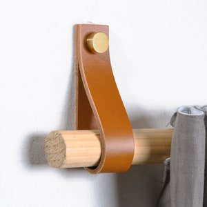 May include: A brown leather curtain tieback with a brass knob attached to a wooden curtain rod.