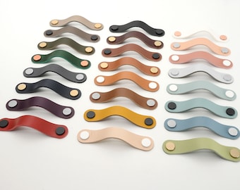 May include: Assortment of 18 leather cabinet pulls in various colors, including red, brown, green, blue, and gray. Each pull has a curved shape and two metal end caps.