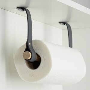 May include: A black leather paper towel holder with a wooden dowel, mounted under a cabinet.