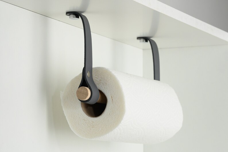 May include: A black leather paper towel holder with a wooden dowel, mounted under a cabinet.