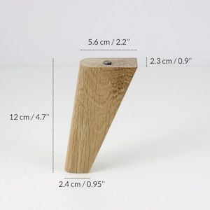 May include: A wooden furniture leg with a tapered design. It measures 12 inches in length, 2.2 inches in width, and 0.95 inches in thickness.