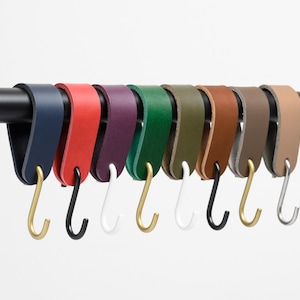 May include: Nine leather keychains with different coloured leather straps and metal hooks. The colours are navy blue, red, purple, green, olive green, brown, grey, and beige.