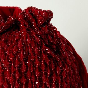 May include: A red beaded drawstring bag with a gathered top. The bag is made of small, teardrop-shaped beads.