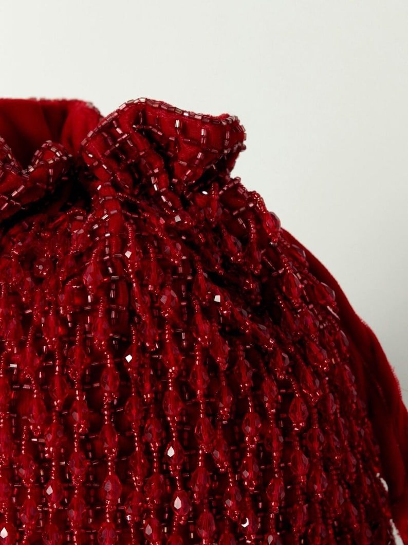 May include: A red beaded drawstring bag with a gathered top. The bag is made of small, teardrop-shaped beads.