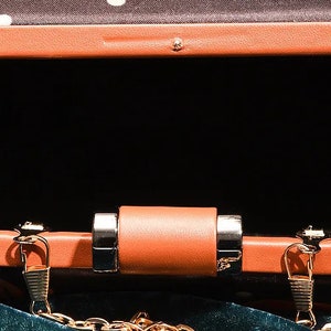 May include: A small, orange, rectangular clutch purse with a gold chain strap. The purse has a black fabric lining and a gold clasp.