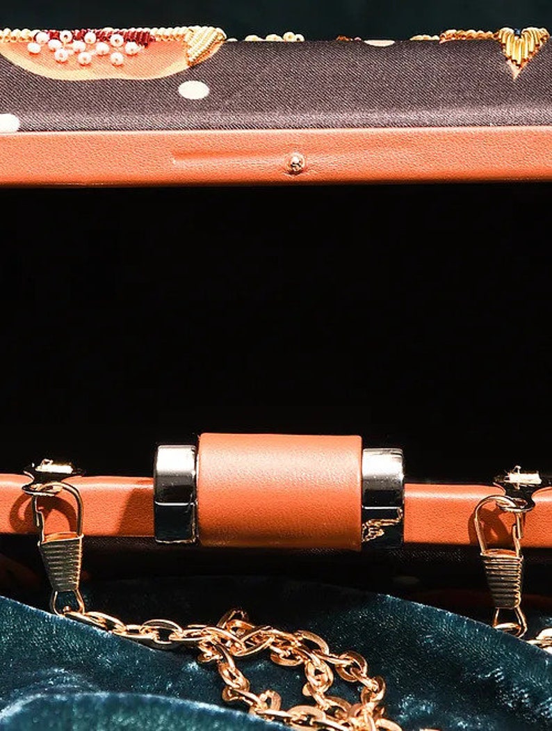 May include: A small, orange, rectangular clutch purse with a gold chain strap. The purse has a black fabric lining and a gold clasp.