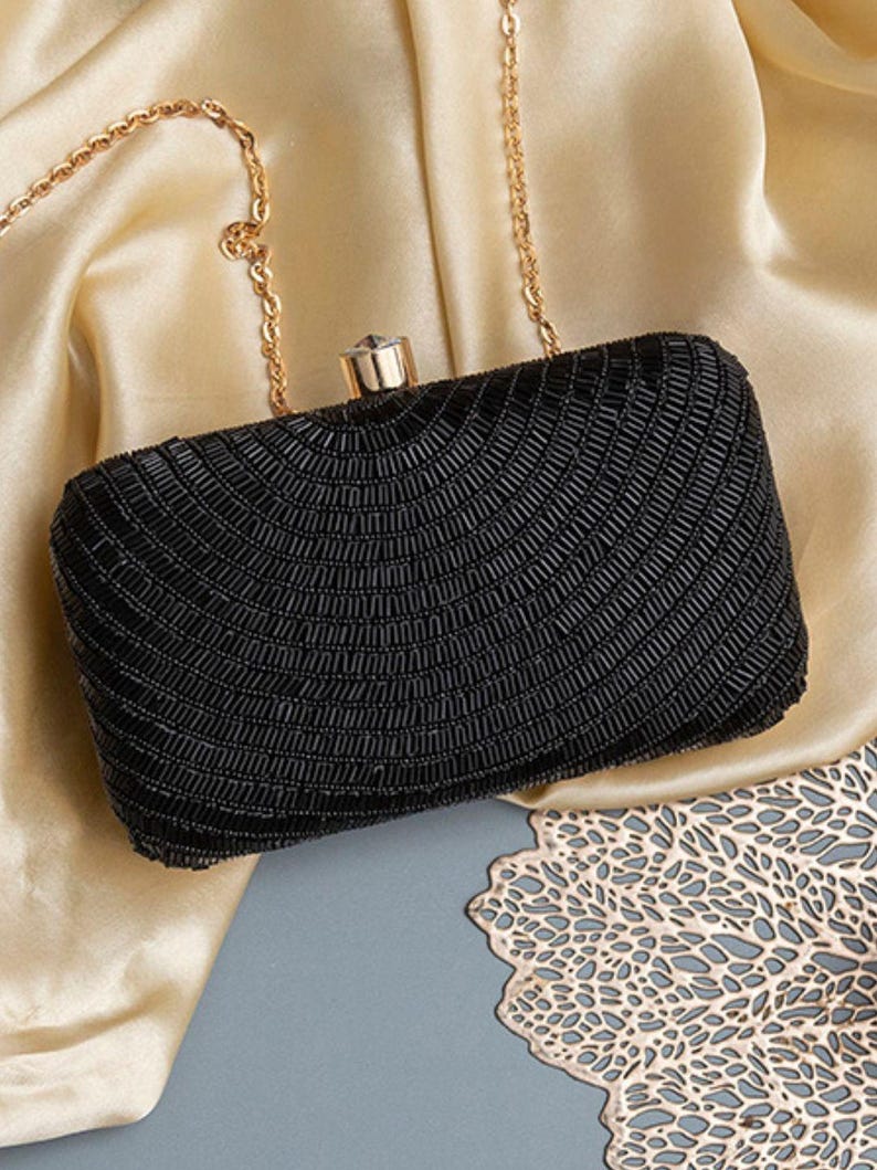 Puede incluir: Un bolso de mano negro de cuentas con una cadena de oro y un cierre de cristal.