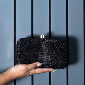 Puede incluir: Un clutch negro de cuentas con un cierre dorado. El clutch es peque&ntilde;o y rectangular.