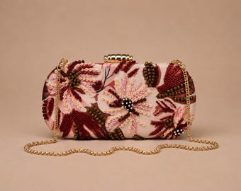Può includere: Una pochette rettangolare con base in raso rosa chiaro e intricati ricami floreali nelle tonalità del rosso scuro, bordeaux e rosa tenue. La borsa presenta una struttura in metallo dorato, una chiusura superiore e una tracolla a catena dorata.