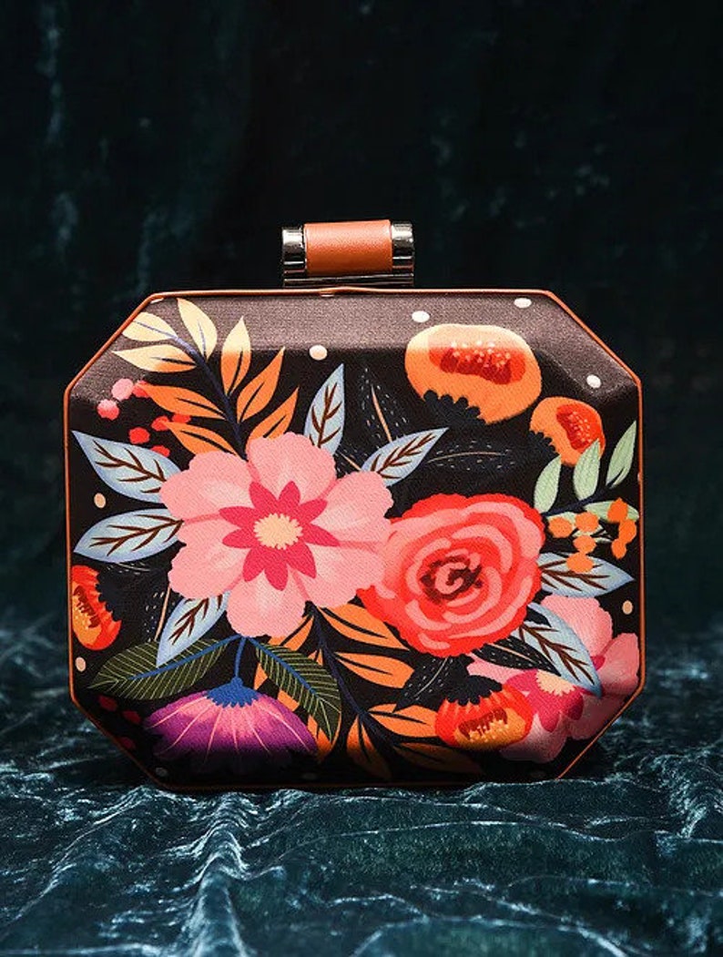 May include: A black clutch purse with a floral print featuring pink, red, orange, and purple flowers on a dark background. The purse has a brown top handle and a silver clasp.