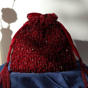 May include: A deep red beaded drawstring bag with a tassel. The bag is made of velvet and is decorated with small, round beads.