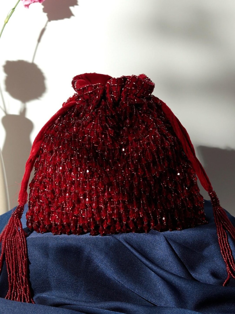May include: A deep red beaded drawstring bag with a tassel. The bag is made of velvet and is decorated with small, round beads.