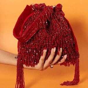 May include: A red beaded drawstring bag with a long tassel. The bag is made of small, red beads and has a velvet strap.