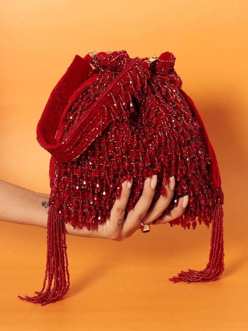 May include: A red beaded drawstring bag with a long tassel. The bag is made of small, red beads and has a velvet strap.