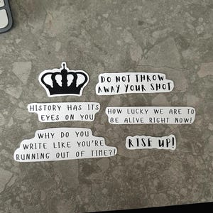 May include: A collection of white stickers with black text. The stickers feature phrases like "Do Not Throw Away Your Shot," "History Has Its Eyes On You," and "Rise Up!" A black and white crown sticker is also included.