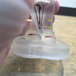 Puede incluir: Una figurita de vidrio transparente de una persona que lleva un sombrero y una chaqueta con detalles amarillos. La figurita est&aacute; de pie sobre una base de vidrio transparente con las palabras "The Franklin Mint" inscritas en la parte inferior.