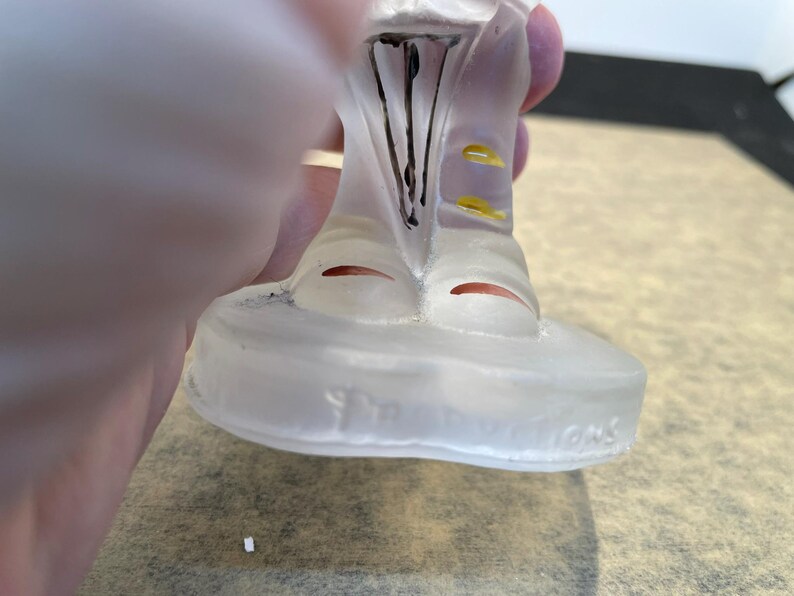 Puede incluir: Una figurita de vidrio transparente de una persona que lleva un sombrero y una chaqueta con detalles amarillos. La figurita est&aacute; de pie sobre una base de vidrio transparente con las palabras "The Franklin Mint" inscritas en la parte inferior.