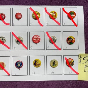 Puede incluir: Una colección de botones vintage con alfiler exhibidos en una hoja blanca. Los botones presentan varios diseños, incluyendo texto y personajes de dibujos animados. La hoja está sobre una superficie morada. Algunos botones tienen líneas diagonales rojas.