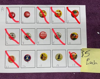 May include: A selection of vintage pin badges displayed on a white sheet. The badges feature various designs, including text and cartoon characters. The sheet is on a purple surface. Some badges have red diagonal lines through them.