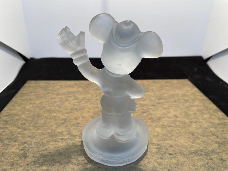 May include: A frosted glass figurine of Mickey Mouse wearing a hat and holding his glove up in the air. The figurine is standing on a round base.