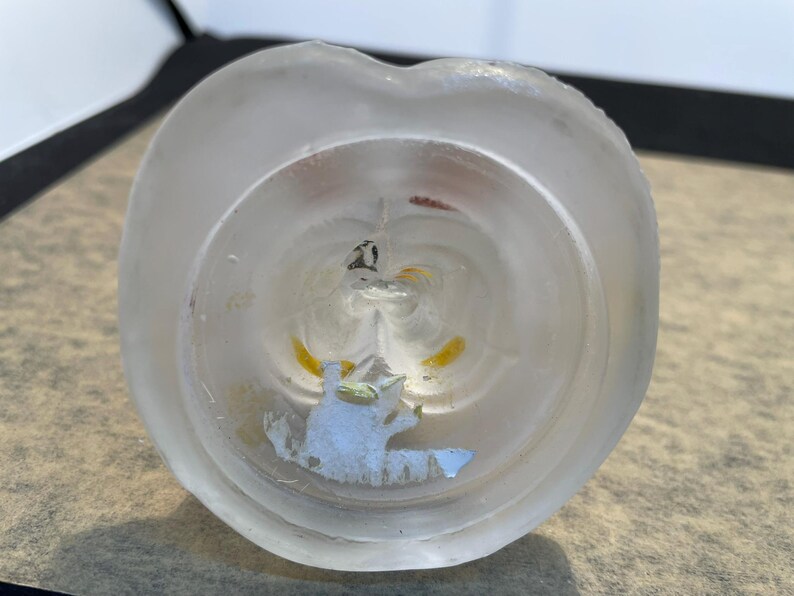 Puede incluir: Un tap&oacute;n de botella de vidrio transparente con un acabado esmerilado. El tap&oacute;n presenta un dise&ntilde;o floral blanco y amarillo con un peque&ntilde;o animal blanco en su interior.