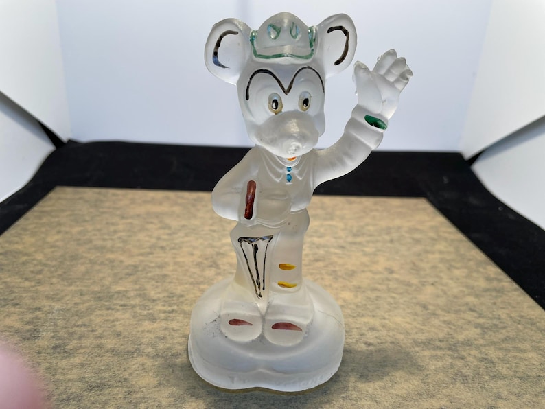 Puede incluir: Una figurita de cristal transparente de Mickey Mouse con un sombrero y un paraguas. La figurita est&aacute; pintada con detalles amarillos, rojos y azules.