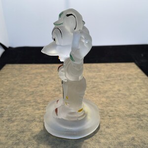 Puede incluir: Una figurita de cristal transparente de un personaje de dibujos animados con un sombrero verde y zapatos rojos. La figurita est&aacute; de pie sobre una base de cristal transparente.