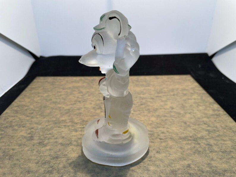 Puede incluir: Una figurita de cristal transparente de un personaje de dibujos animados con un sombrero verde y zapatos rojos. La figurita est&aacute; de pie sobre una base de cristal transparente.