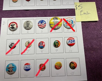 May include: A collection of vintage pinback buttons, each with a unique design. The buttons feature images of political figures, cartoon characters, and other graphics. The buttons are arranged on a white sheet with a purple background.