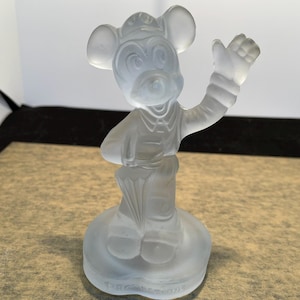 May include: A frosted glass figurine of Mickey Mouse wearing a hat and holding an umbrella. The figurine is standing on a circular base.