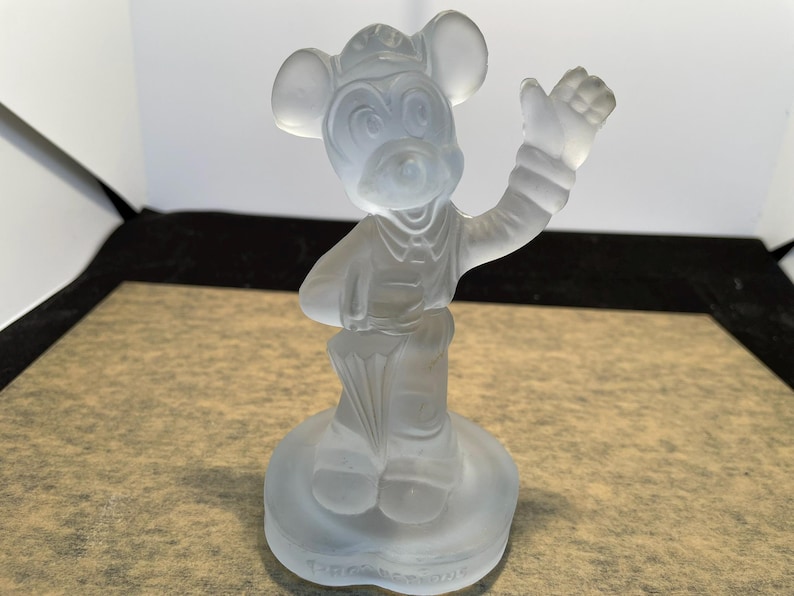 May include: A frosted glass figurine of Mickey Mouse wearing a hat and holding an umbrella. The figurine is standing on a circular base.