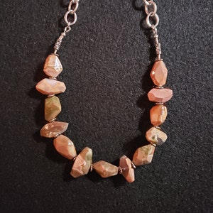 May include: A necklace made with a silver chain and brown, green, and white agate stones.