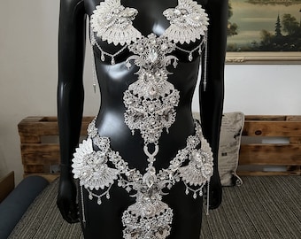May include: A silver body chain with crystal embellishments. The chain features a delicate, intricate design with a floral motif. The chain is made up of multiple pieces that can be worn together or separately.