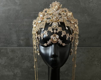 May include: A gold crown with crystal embellishments and dangling chains. The crown is on a black mannequin head.