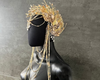 May include: A gold and brown beaded headpiece with a long chain of beads hanging down the back. The headpiece is made of wire and beads, and it has a delicate, intricate design.