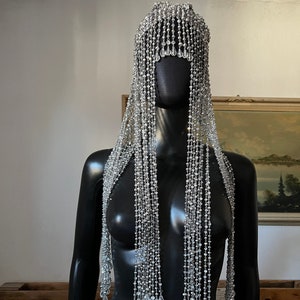 May include: A silver beaded headpiece with long strands of crystal beads hanging down. The headpiece is on a black mannequin.