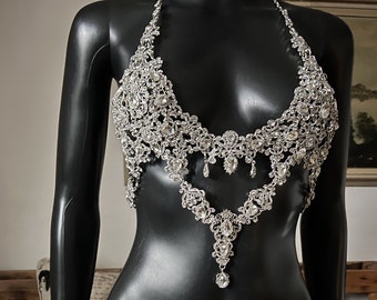 May include: A silver-toned body chain with a delicate, intricate design featuring numerous small rhinestones. The chain is designed to be worn as a bra top and has a dangling pendant.