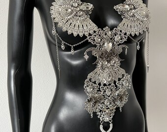 May include: A silver body chain with a delicate, intricate design featuring a crescent moon and star motif. The chain is adorned with numerous clear rhinestones and has a dangling pendant.