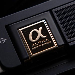 Könnte beinhalten: Nahaufnahme einer schwarzen Kamera mit einem goldfarbenen "ALPHA"-Logo mit einem Filmstreifen-Design. Das Logo lautet "SONY α-mount".