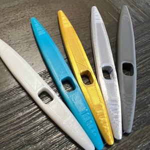May include: Five plastic knitting needles in different colors: white, blue, gold, silver, and gray. The needles are all the same size and shape, with a small hole in the middle.