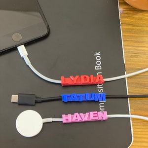 May include: Three white cords with colorful 3D printed labels that say "LYDIA", "TATUM", and "HAVEN". The cords are plugged into a laptop and a phone.