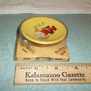 May include: A yellow and red wooden toy train knob in a plastic package. The package has the text "Story Book Knobs" and "A602" printed on it.