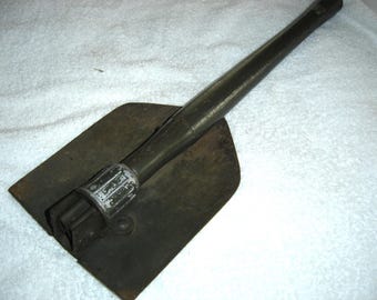 May include: A vintage folding shovel with a dark green handle and a square, dark metal blade. The handle is made of metal and has a textured grip. The shovel is designed to fold for compact storage.