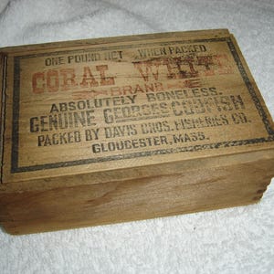 May include: A wooden box with a label that reads "One Pound Net When Packed Coral White Brand Absolutely Boneless Genuine Georges Codfish Packed by Davis Bros. Fisheries Co. Gloucester, Mass."