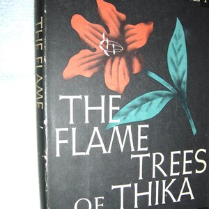 May include: A hardcover book titled "The Flame Trees of Thika" by Elspeth Huxley. The cover features a large orange flower with teal leaves against a black background. The title is in white, with the subtitle "Memories of an African Childhood".