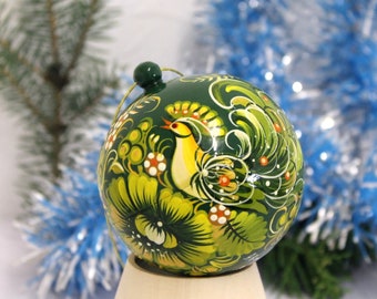 May include: A green Christmas bauble with a painted design of a bird and flowers. The bauble is hand-painted with intricate details and vibrant colours.